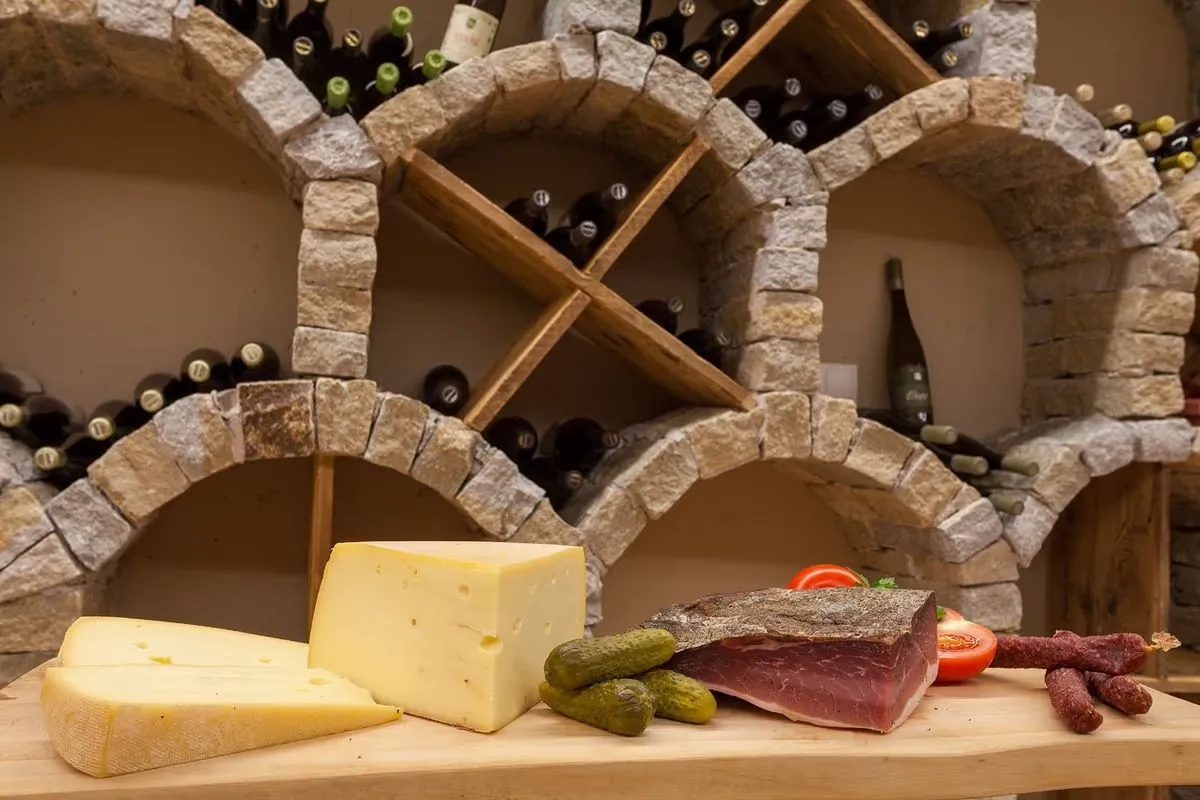 Bogennischen aus Stein voller Weinflaschen, davor Käse und Speck